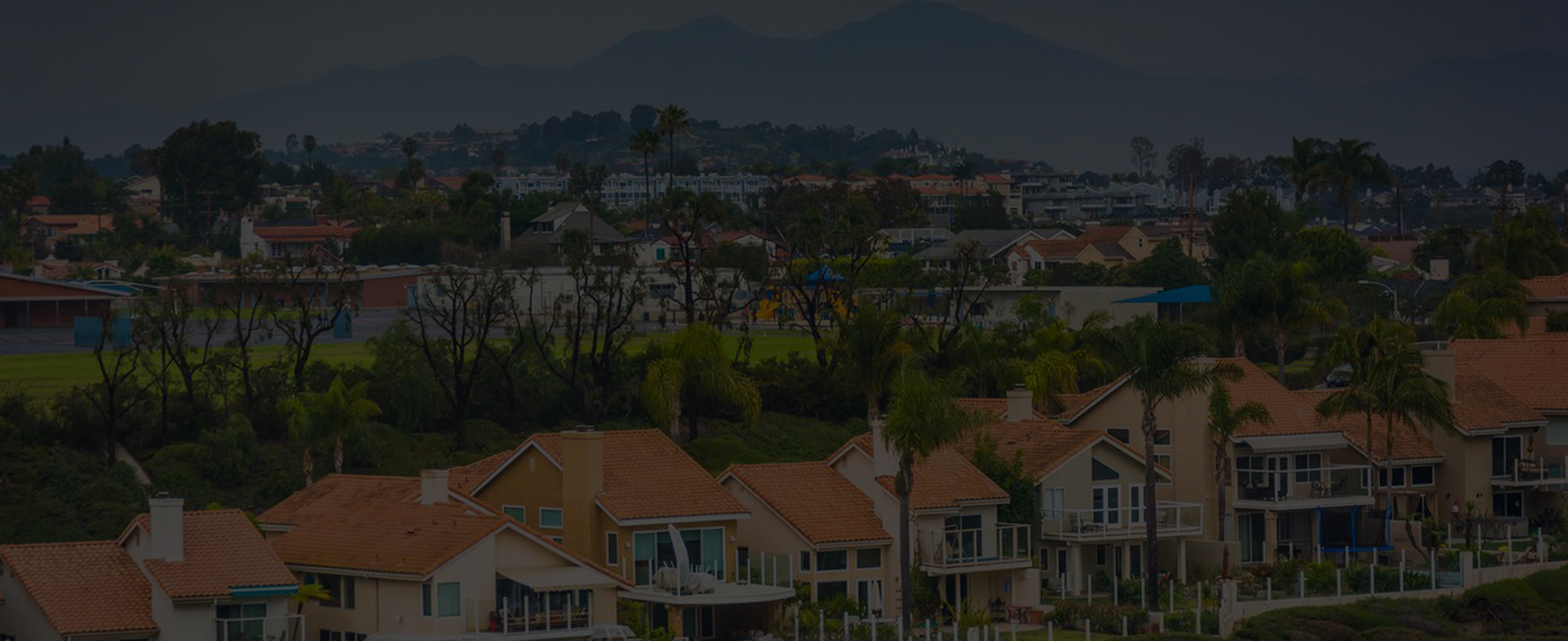 Panoramic view of a serene residential area serviced by Garden Home Inspection, with two-story homes sporting terracotta roofs amidst lush greenery and rolling hills in the background, reflecting the area and communities we serve.