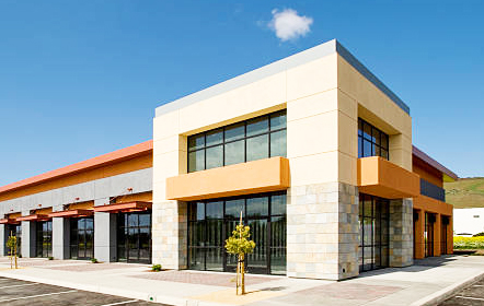 Modern strip mall with a distinctive beige and orange façade and large windows, under a clear blue sky with green hills in the background, indicative of the type of properties Garden Home Inspection specializes in inspecting.