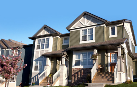 Two-story green multi-family home with white trim and personal touches on the front porches, under a clear blue sky, showcasing a potential for a vibrant community post home inspection.