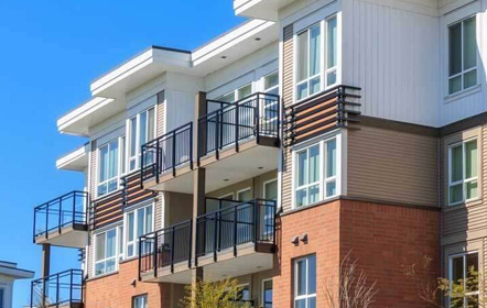 Modern condominium building with red brick and beige paneling, featuring private balconies with black railings, representative of the type of residences Garden Home Inspection services, under a bright blue sky.