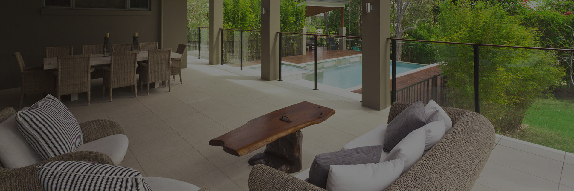 Elegant outdoor patio adjoining a serene swimming pool, furnished with woven dining and lounge sets, and offering a clear view of the surrounding verdant landscape, symbolizing a home’s luxurious leisure space post home inspection.